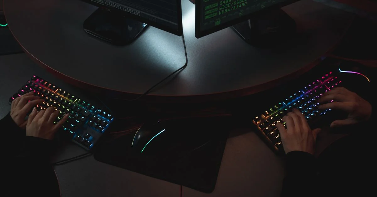 Deux personnes tapant sur des claviers RGB avec du code sur les écrans, indiquant un environnement de cybersécurité.