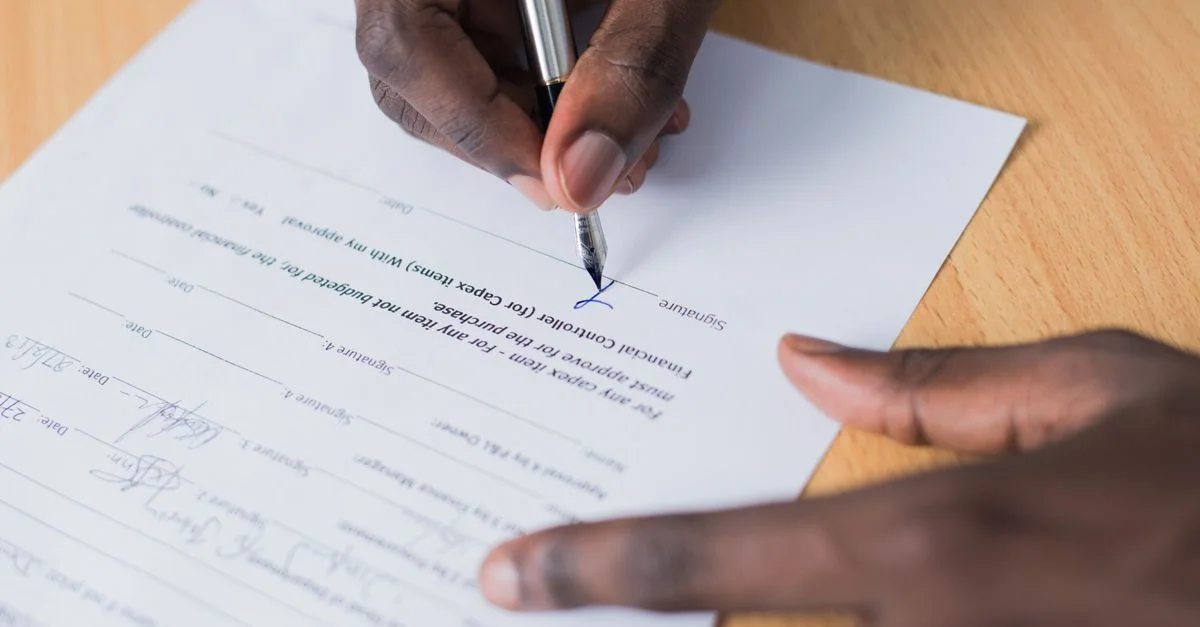 Vue en gros plan de la main d'une personne signant un contrat commercial sur un bureau avec un stylo.