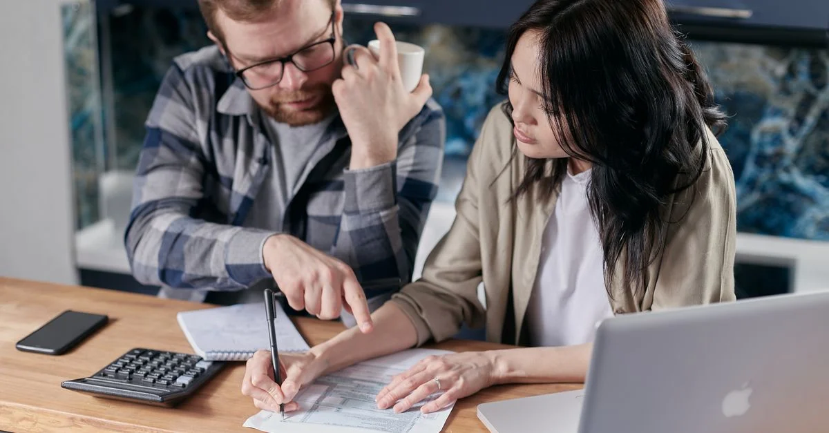 Un couple analysant des documents financiers avec une calculatrice et un ordinateur portable sur une table.